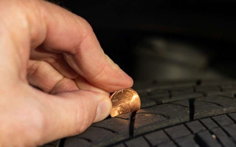 Person checking tire wear using the penny method